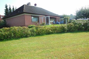 Ein Ziegelhaus mit überdachter Veranda, Rasen und einer Hecke.