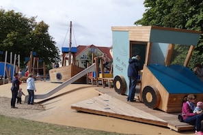 Ein Spielplatz mit einer Rutsche, einer hölzernen Schiffkonstruktion und einer Rampe.