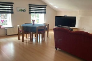 A room with a dining table, chairs, a red sofa, a TV, and a window with blinds. - at the Harnisch holiday farm (Westerholz)