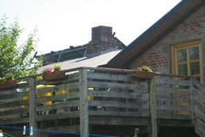 A rustic building with a wooden balcony, brick chimney, and a window with a wooden frame. - at the Harnisch holiday farm (Westerholz)