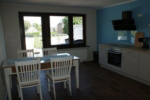 Una cocina con alacenas blancas, una estufa y un ventanal con vista a casas.