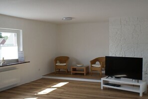 Ein Wohnzimmer mit Fernseher, zwei Korbstühlen, einem kleinen Tisch und einer Wand mit Steinoptik.