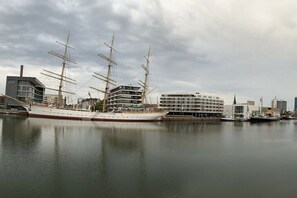 Ein großes Segelschiff liegt in einer Marina vor modernen Gebäuden.