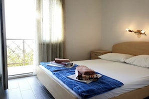 Ein Hotelzimmer mit Bett, Nachttisch, Wandleuchte und Blick durch ein Fenster.
