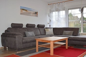 Ein modernes Wohnzimmer mit einem grauen Ecksofa, einem Holztisch und einem roten und grauen Teppich.