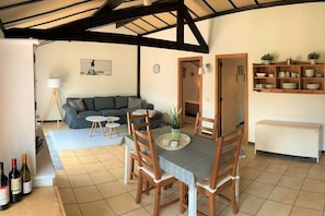 A dining area with a table set for four, a sofa, a lamp, and a shelf with dishes.