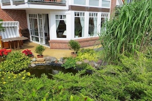 Ein Wohngebäude mit Terrasse, einem kleinen Teich und verschiedenen Pflanzen.