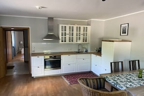 Eine kleine Küche mit weißen Schränken, einem Einbauofen und einem Essbereich mit Tisch und Stühlen.