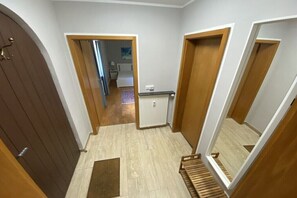 Ein Flur mit Holztüren, einem Heizkörper und Blick in ein Schlafzimmer mit Bett und Nachttisch.