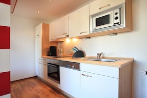 A compact kitchen with white cabinets, a built-in microwave, a dishwasher, and a wooden countertop. - Holiday apartment with 1 bedroom (Borkum)