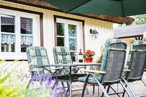 Eine Terrasse mit vier Stühlen, einem Tisch und einem grünen Sonnenschirm.