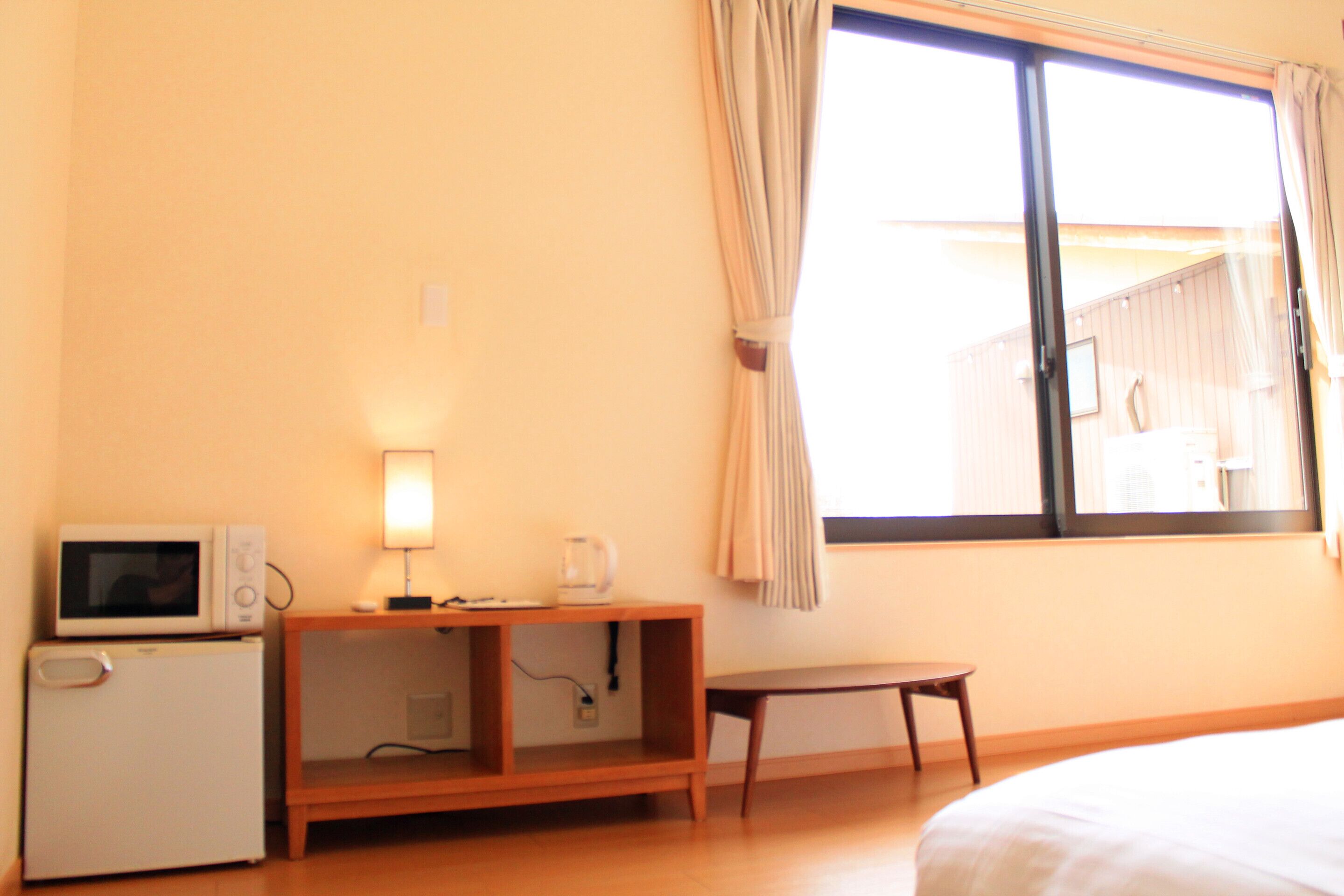A hotel room with a bed, a small table, a microwave, a lamp, and a window with curtains.