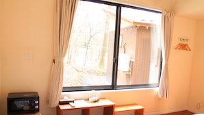 Una habitación con una cama, un escritorio pequeño con un microondas, un banco y una ventana con cortinas.