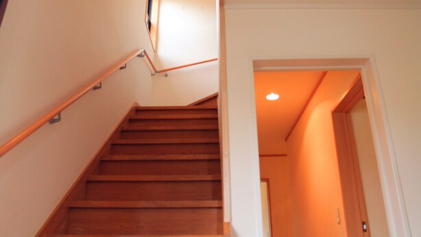 Una escalera de madera con barandilla que conduce a una habitación con una puerta y un aplique en el techo.