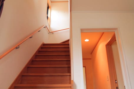 A wooden staircase with a handrail, leading to a room with a door and a light fixture on the ceiling.
