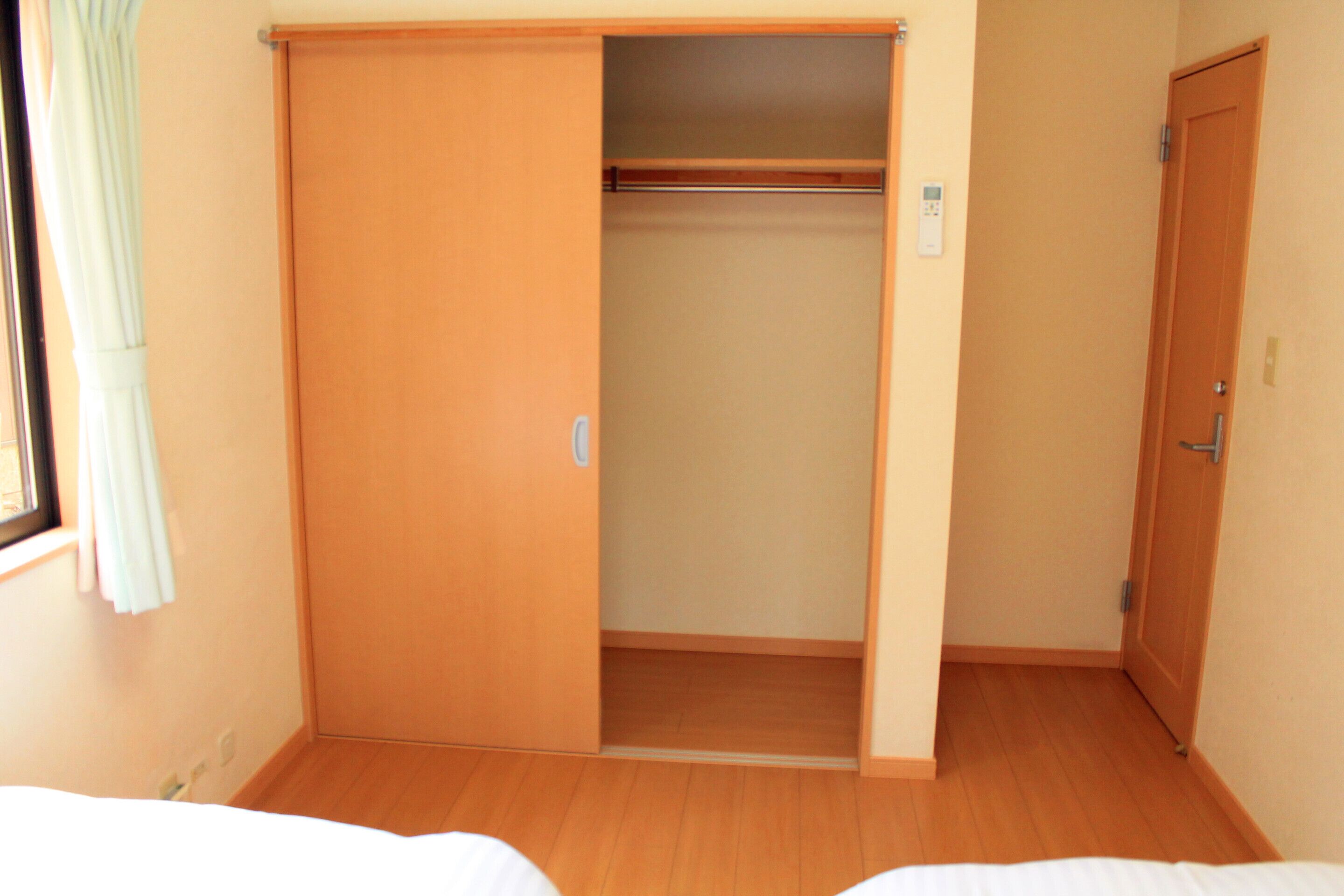Une pièce avec un plancher en bois, un placard avec une porte coulissante et une fenêtre avec des rideaux.