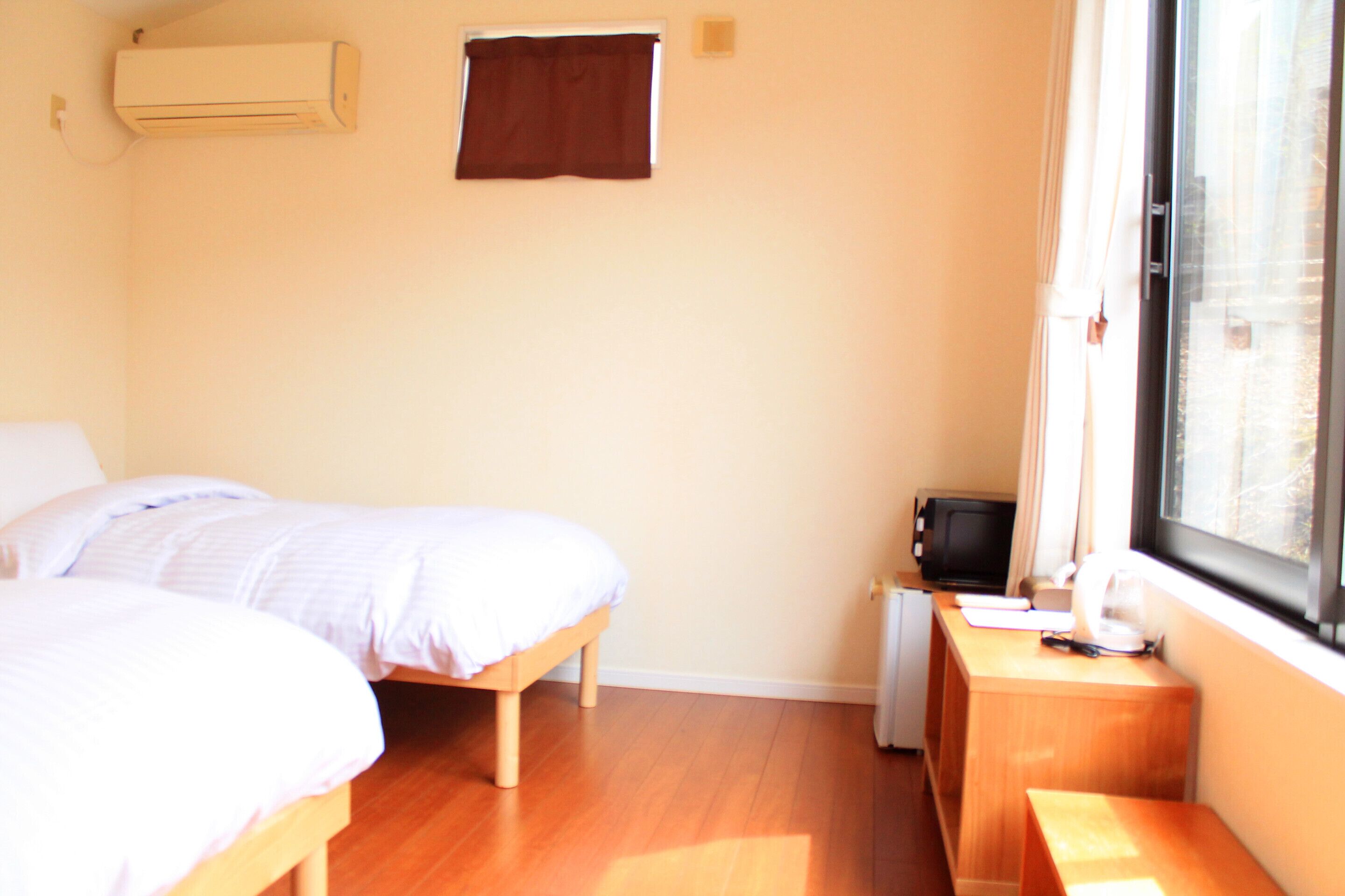 A bedroom with a bed, a desk, a chair, a window, and a wall-mounted air conditioner.