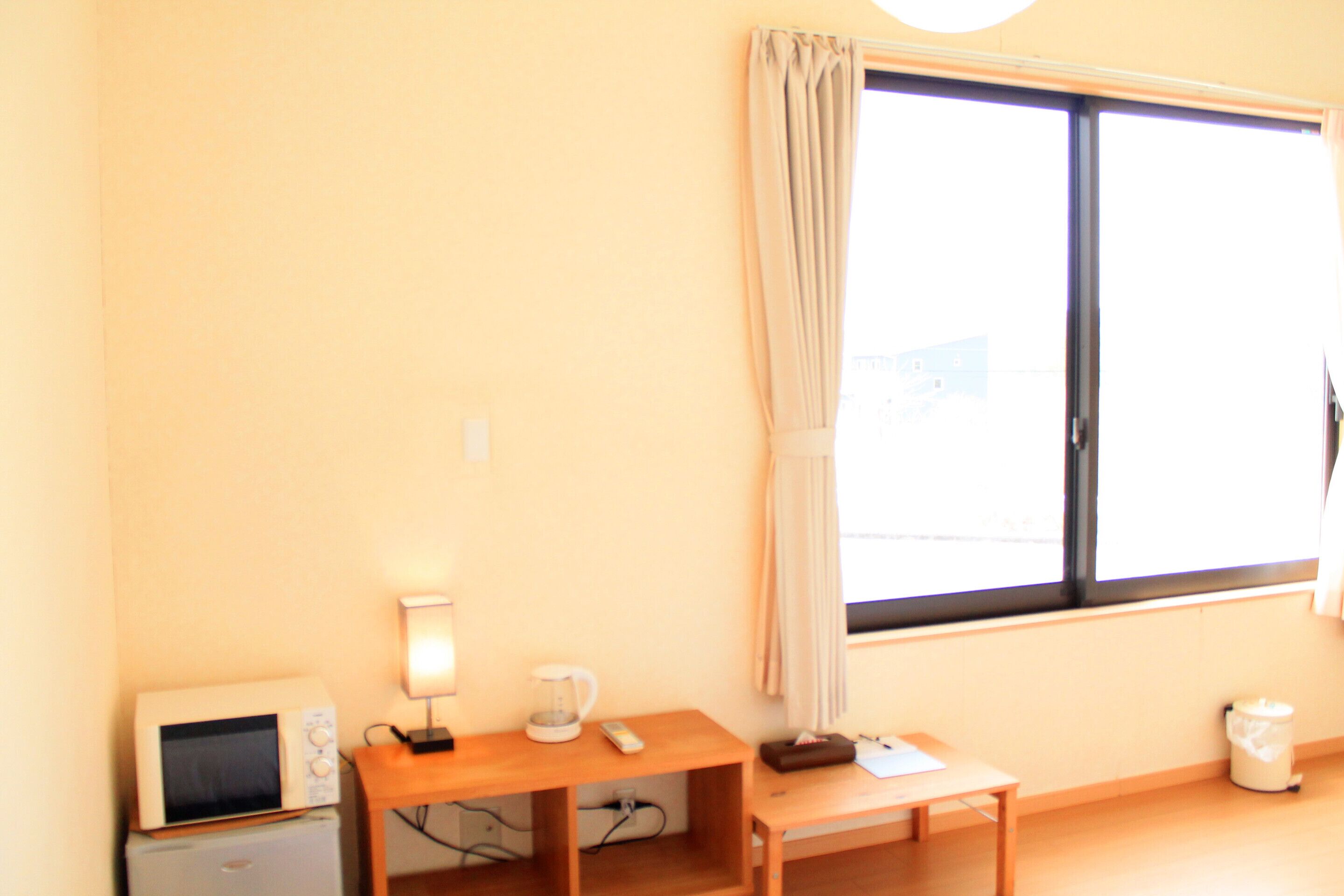 A room with a small table, a microwave, a coffee maker, and a window with curtains.