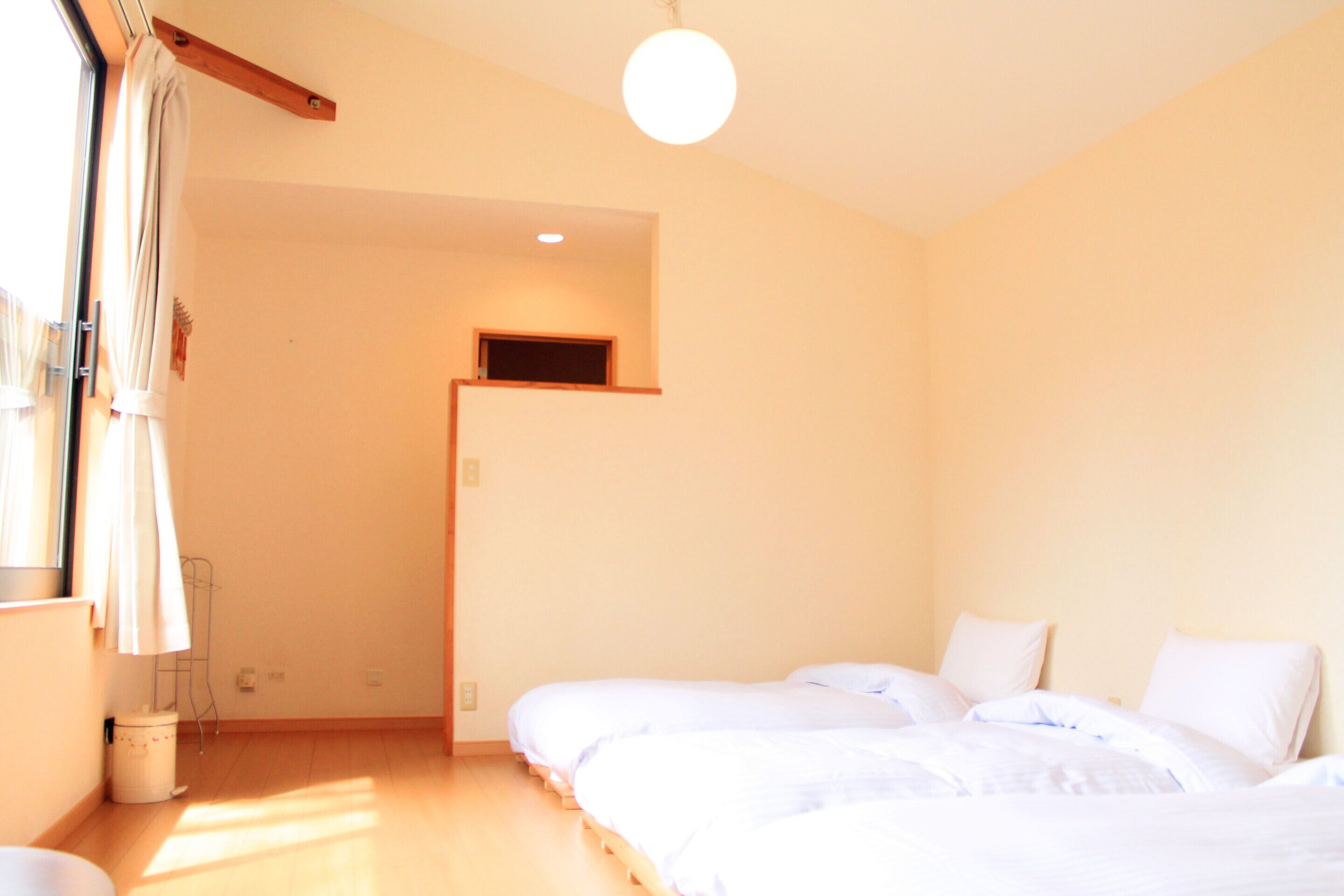 A bedroom with two beds, a window with curtains, a small skylight, and a wooden beam ceiling.