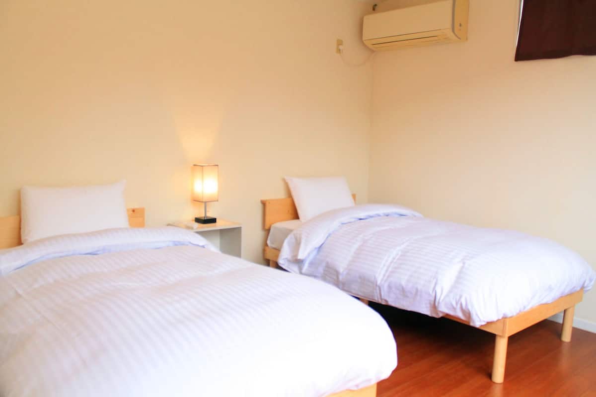 A room with two beds, a bedside table with a lamp, and an air conditioning unit on the wall.