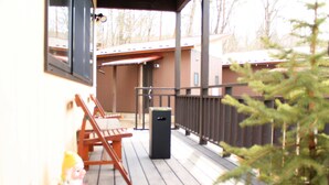 Una terraza de madera con barandilla de metal, un cubo de basura y un pequeño árbol de Navidad.