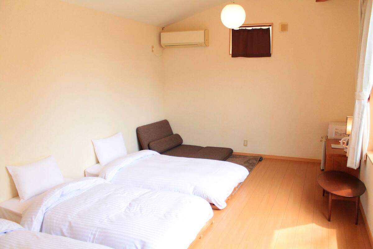 A room with two beds, a chair, a desk, and an air conditioning unit.