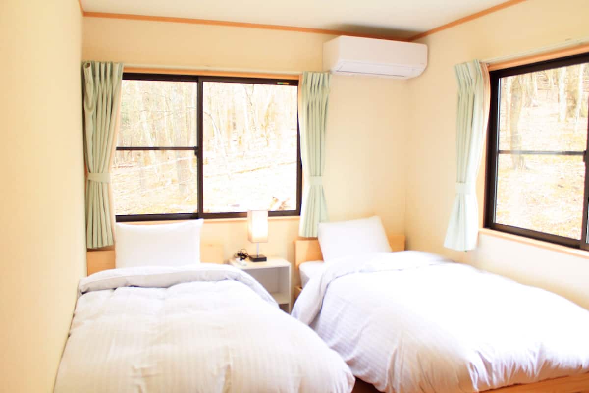 A room with two beds, a small table, a lamp, and an air conditioning unit.