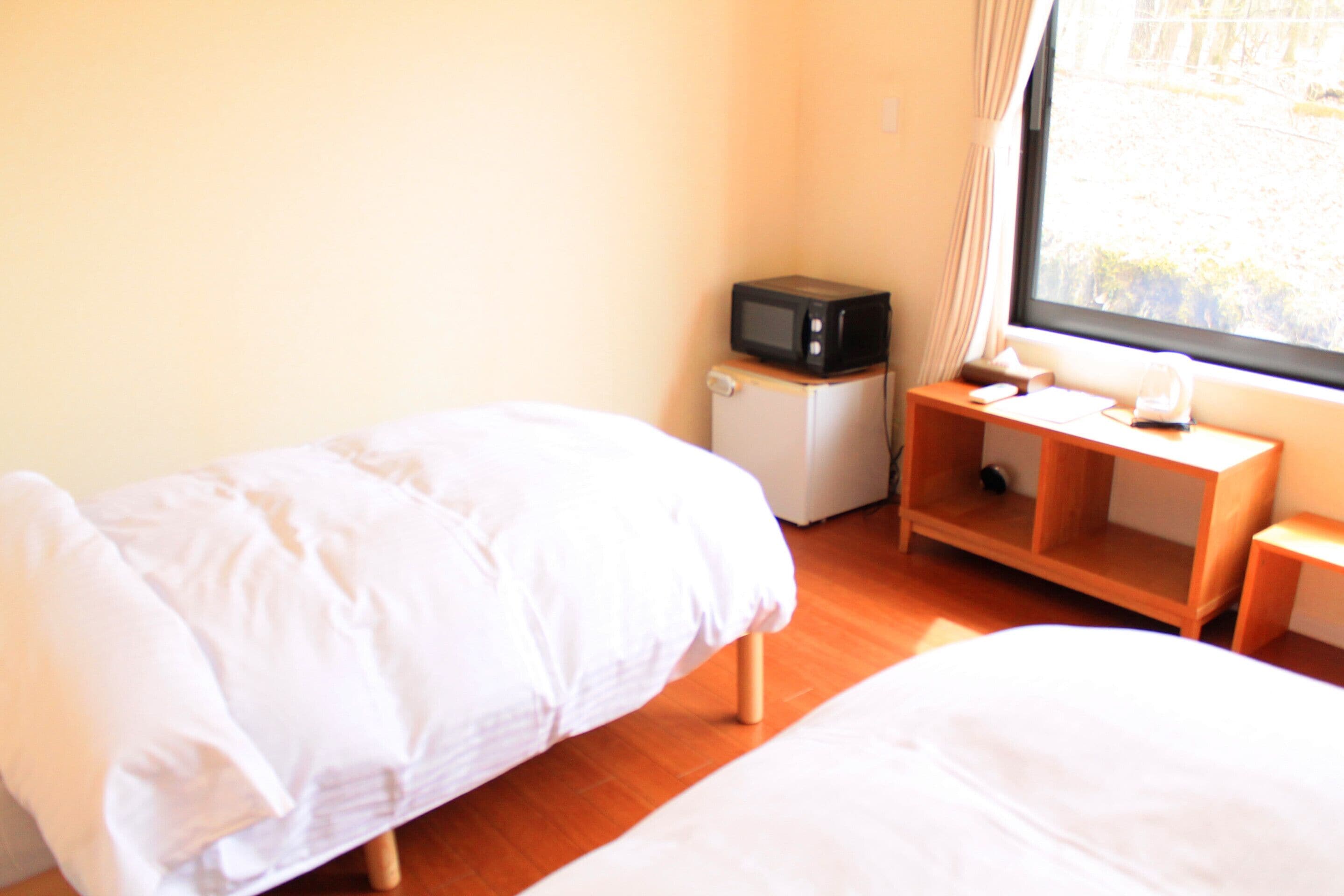 Une chambre avec deux lits, un petit bureau équipé d’un micro-ondes et une fenêtre avec des rideaux.