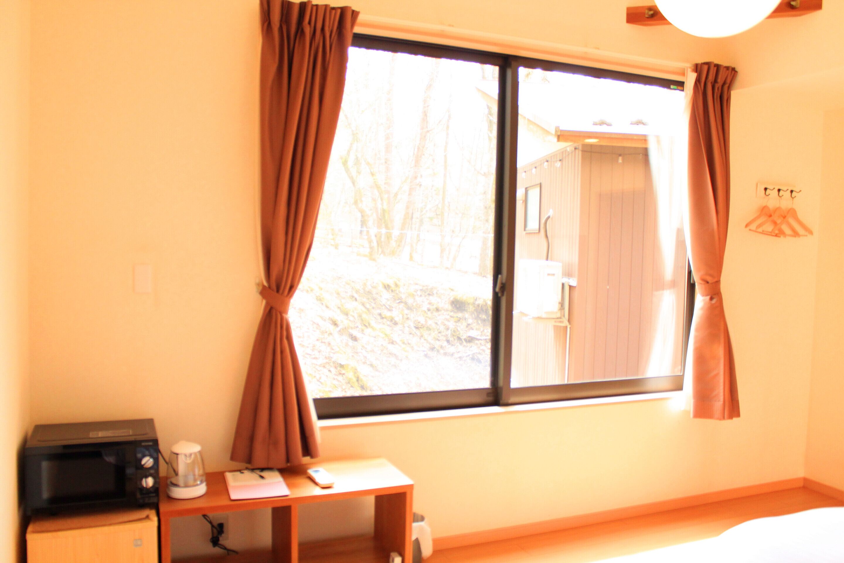 A room with a window, a desk with a microwave, and a small cabinet.