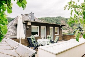 A covered outdoor patio with a table and chairs, a white umbrella, and a view of a hillside. - Holiday apartment with 1 bedroom (Cochem)