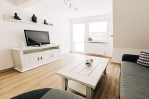 A modern living room with a flat-screen TV, white cabinetry, a coffee table, and a sofa. - Holiday apartment with 1 bedroom (Cochem)