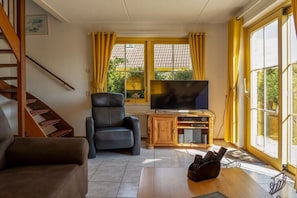 Una sala de estar con un sofá, una silla, un televisor y un mueble de madera.