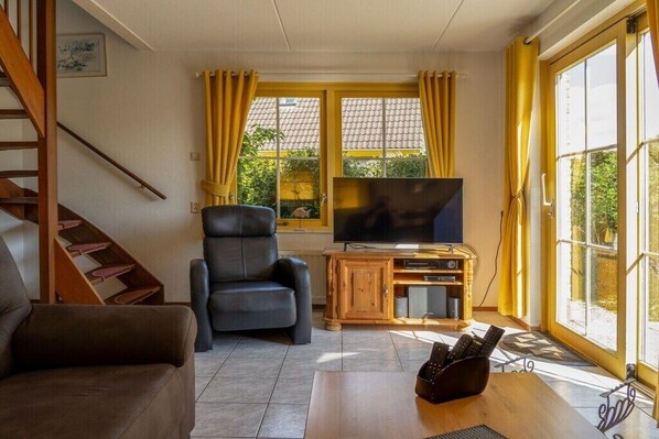 A living room with a sofa, a chair, a TV, and a wooden cabinet. - Holiday home Strandperle 174 (Julianadorp)