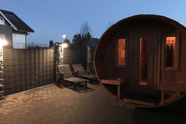 A wooden barrel-shaped structure with a door, two chairs, and a table in a backyard setting. - Holiday home with 4 bedrooms (Winterberg)