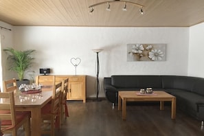 A modern living room with a dining table, chairs, a black sofa, a coffee table, a floor lamp, a potted plant, and a wall art piece. - Holiday home with 4 bedrooms (Winterberg)