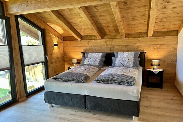 A wooden-paneled bedroom with a bed, two bedside lamps, and a window with blinds.