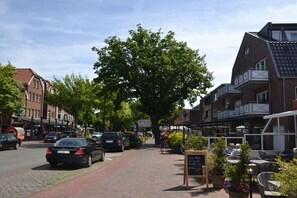 Eine Straße mit parkenden Autos, einem von Bäumen gesäumten Bürgersteig und einem Gebäude mit Außenbestuhlung.