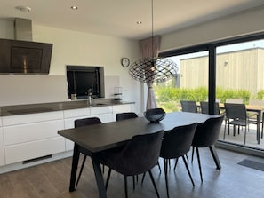 Een moderne keuken met een eethoek, grote ramen en uitzicht op groen.