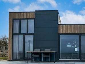 Een modern gebouw met grote ramen, een houten gevel en een bankje ervoor.