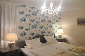 A bedroom with a bed, two bedside tables with lamps, a chandelier, and floral wallpaper. - Müller 3 in the house Spring (Aschau im Chiemgau)
