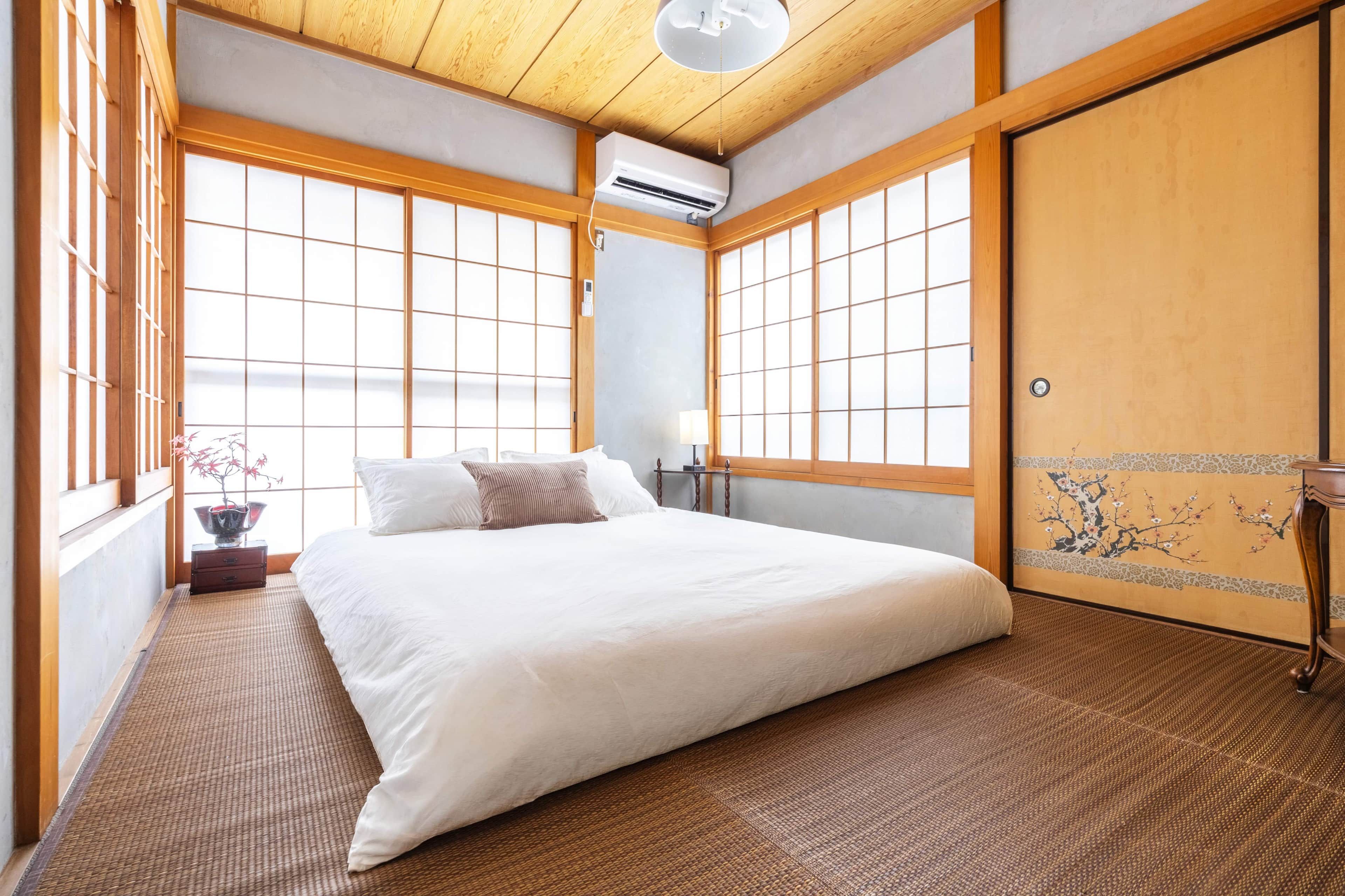 A traditional Japanese-style bedroom with tatami flooring, a bed with white bedding, and a sliding shoji door.