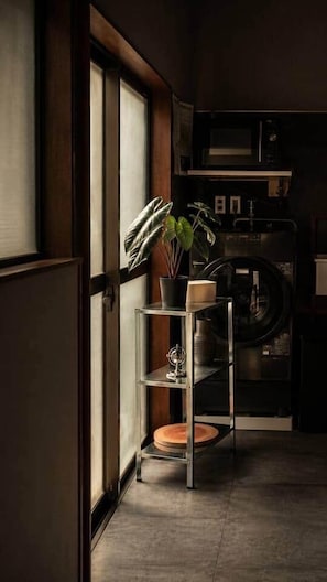 A kitchen with a microwave, a plant on a shelf, and a washing machine in the background. - Skytree Next Door | Modern Ryokan in Tokyo (Katsushika City)