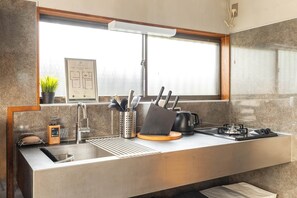 A modern kitchen with a stainless steel sink, a window above the counter, and a fire escape route sign. - Skytree Next Door | Modern Ryokan in Tokyo (Katsushika City)