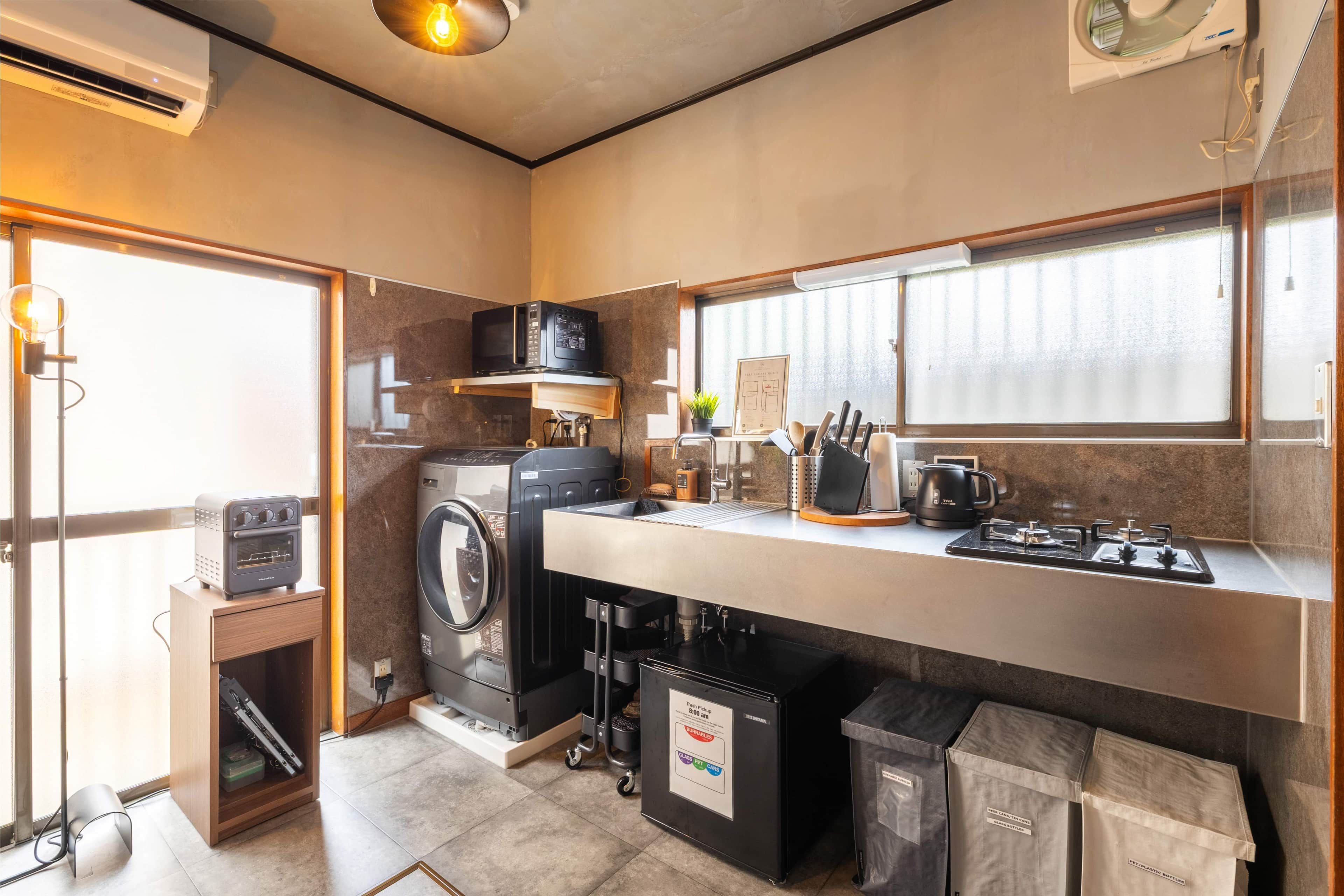 A compact kitchen with a washing machine, microwave, toaster, sink, and a trash bin.