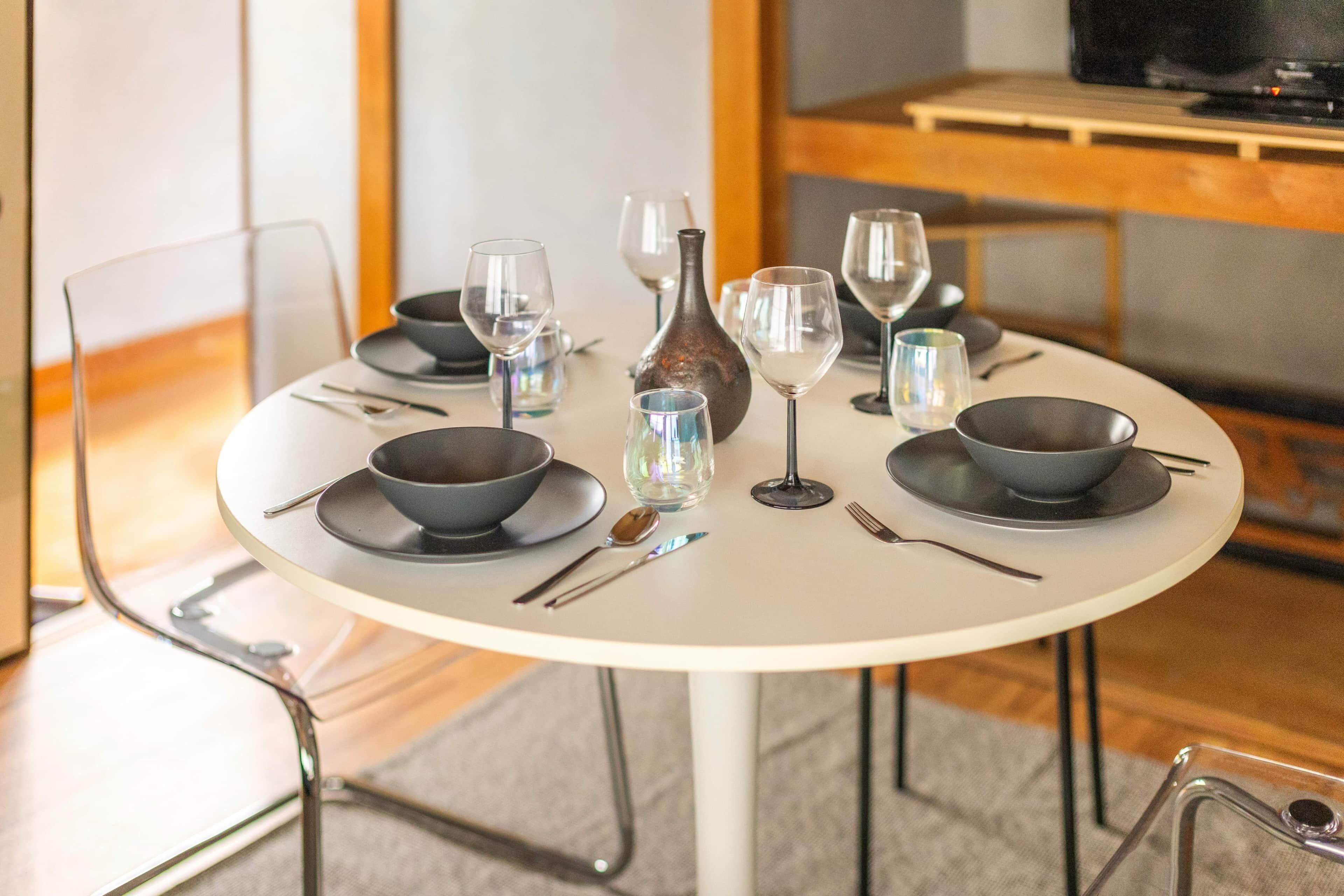 A round dining table with black bowls, wine glasses, and cutlery.