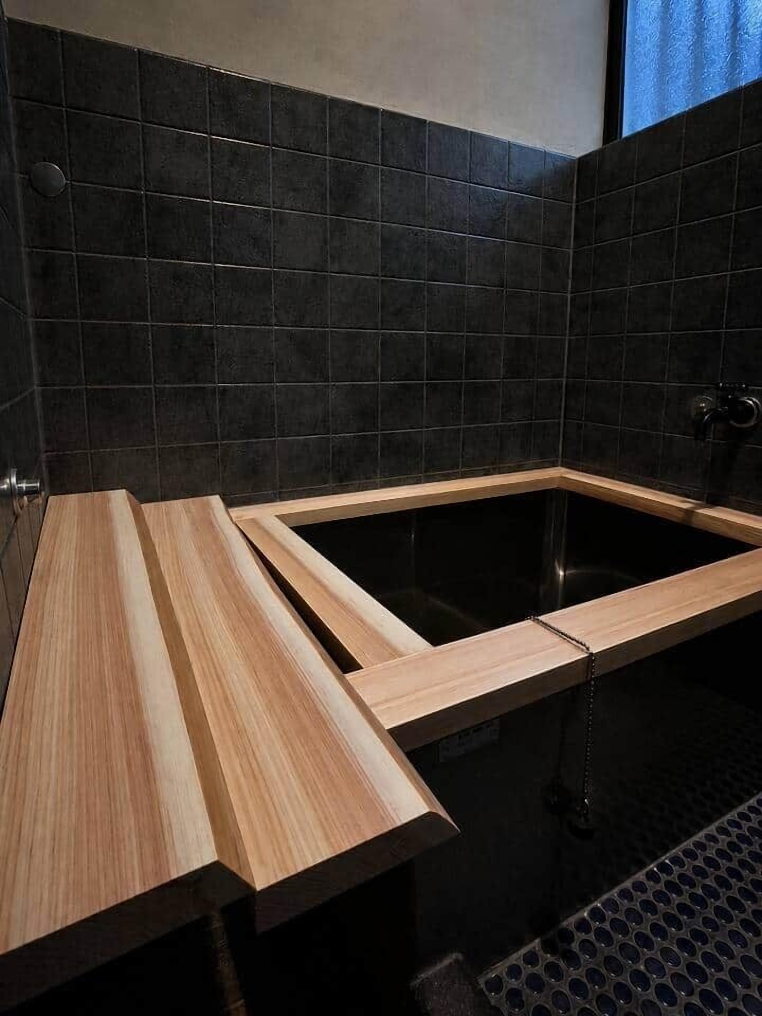 A modern bathroom with a wooden vanity, a black bathtub, and a shower area.