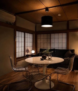 A traditional Japanese-style room with tatami flooring, a round table with chairs, a low ceiling with wooden beams, and sliding shoji screens. - Skytree Next Door | Modern Ryokan in Tokyo (Katsushika City)