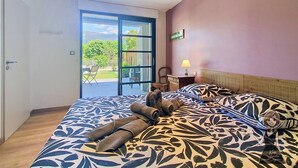 A bedroom with a bed, a nightstand, a lamp, and a sliding glass door leading to an outdoor area. - The Pyrenean Stopover • Between Lourdes and Cauterets. (Argelès-Gazost)