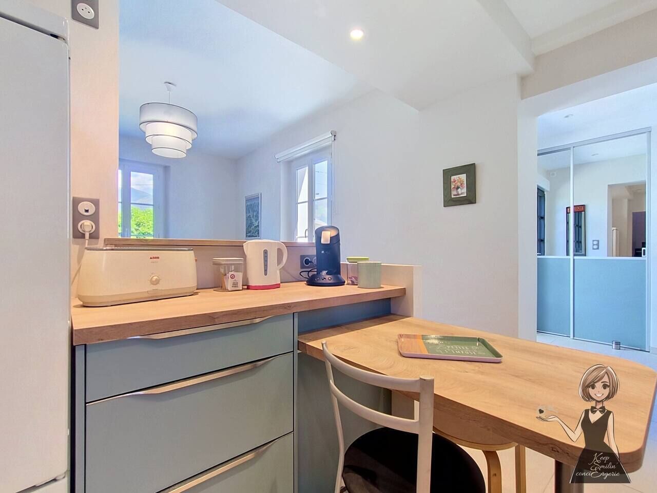 A modern kitchen with a wooden countertop, a kettle, a coffee maker, and a toaster. There is a dining table with a chair and a decorative item on it.