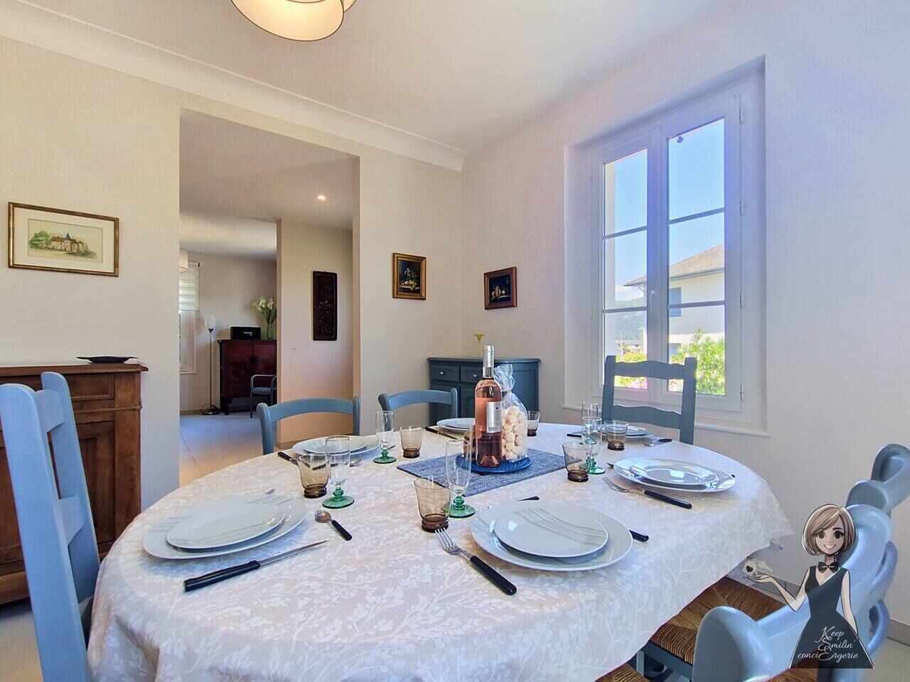 A dining area with a round table set for four, a bottle of wine, and framed pictures on the walls.